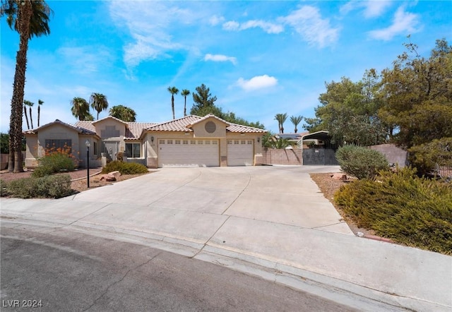 mediterranean / spanish home with a garage, concrete driveway, a tiled roof, fence, and stucco siding