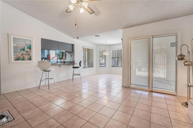 spare room with visible vents, light tile patterned flooring, vaulted ceiling, ceiling fan, and a textured ceiling