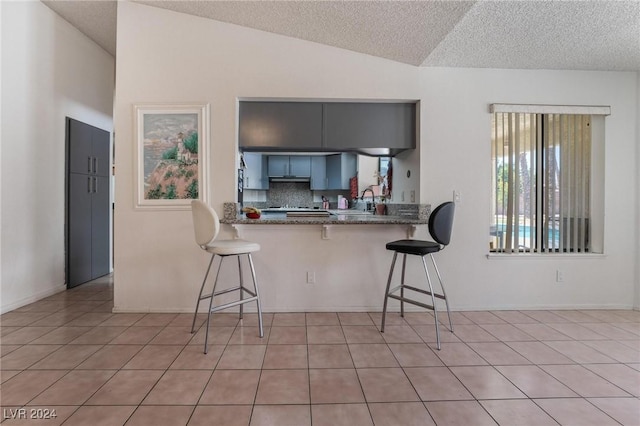 kitchen featuring a breakfast bar, vaulted ceiling, a sink, and light tile patterned floors