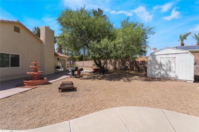 view of yard with a patio, an outdoor fire pit, a fenced backyard, an outdoor structure, and a shed