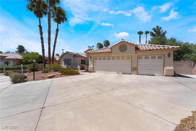 mediterranean / spanish-style home with an attached garage, fence, a tile roof, driveway, and stucco siding