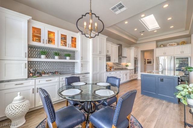 dining area with a chandelier, light wood-style flooring, a skylight, visible vents, and a raised ceiling