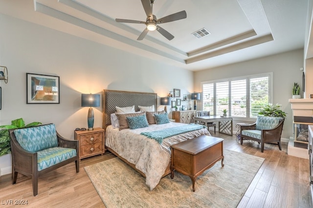 bedroom with a glass covered fireplace, a raised ceiling, visible vents, and light wood finished floors