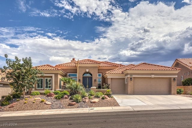 mediterranean / spanish house featuring an attached garage, a tile roof, driveway, stucco siding, and a chimney