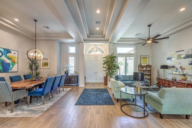 living room with a towering ceiling, a tray ceiling, ceiling fan with notable chandelier, and light wood-type flooring