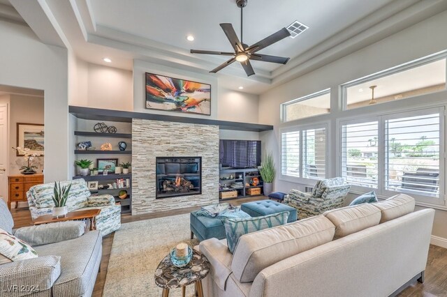 living room with ceiling fan, a fireplace, hardwood / wood-style floors, and a high ceiling