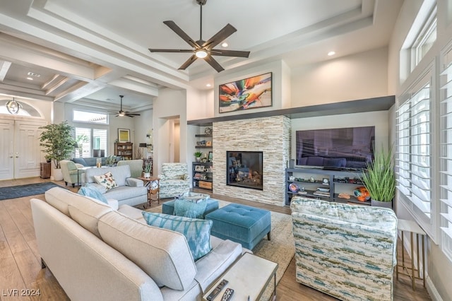 living area featuring light wood-type flooring, a raised ceiling, a ceiling fan, and a stone fireplace