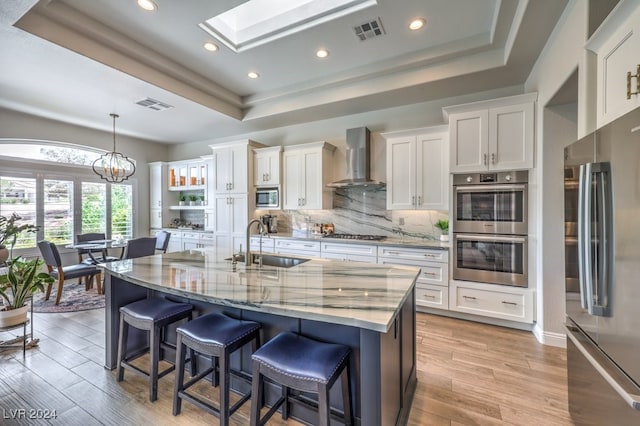 kitchen with appliances with stainless steel finishes, a tray ceiling, white cabinets, and wall chimney exhaust hood