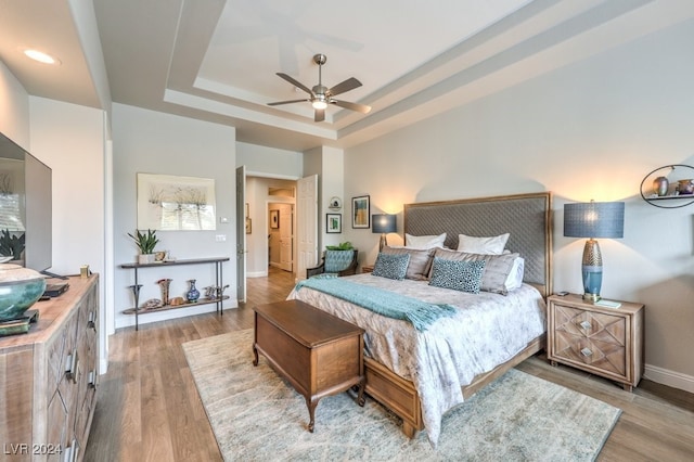 bedroom featuring a raised ceiling, ceiling fan, baseboards, and wood finished floors