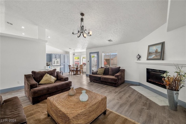 living room with light hardwood / wood-style flooring, a chandelier, lofted ceiling, and a textured ceiling