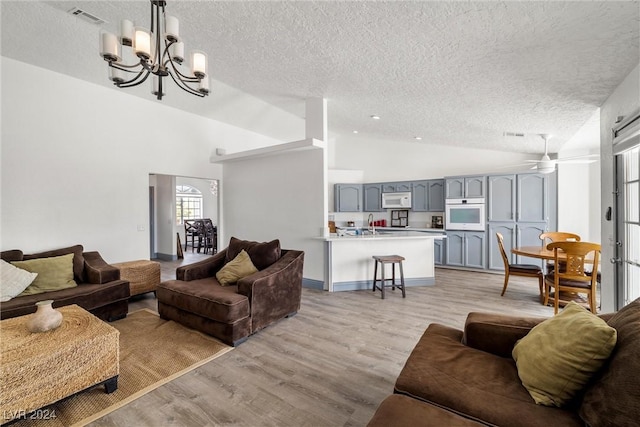 living room with high vaulted ceiling, light wood-type flooring, a textured ceiling, and ceiling fan with notable chandelier