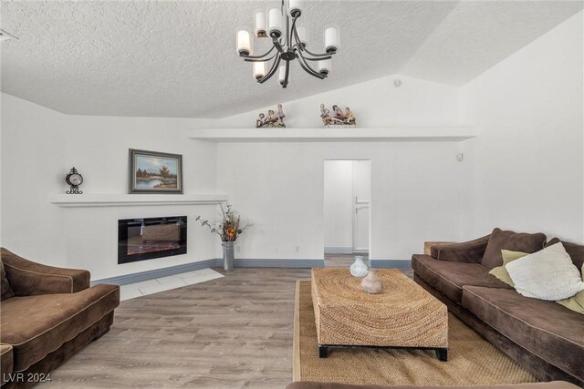 living room with a textured ceiling, vaulted ceiling, a chandelier, and light hardwood / wood-style floors