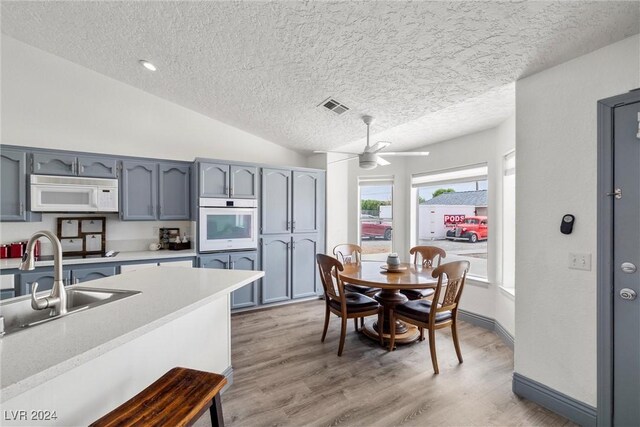 kitchen with a textured ceiling, ceiling fan, hardwood / wood-style flooring, vaulted ceiling, and white appliances