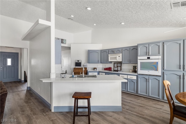 kitchen featuring dark hardwood / wood-style flooring, kitchen peninsula, sink, white appliances, and a breakfast bar area