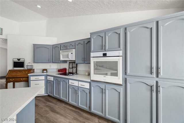 kitchen with white appliances, vaulted ceiling, a textured ceiling, and hardwood / wood-style flooring