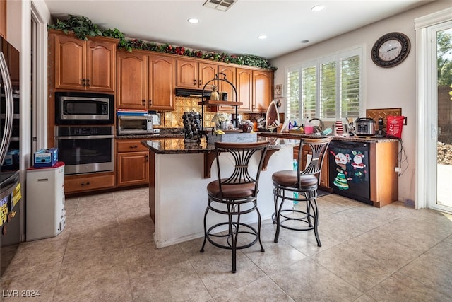 kitchen featuring stainless steel appliances, a kitchen bar, dark stone counters, and a healthy amount of sunlight