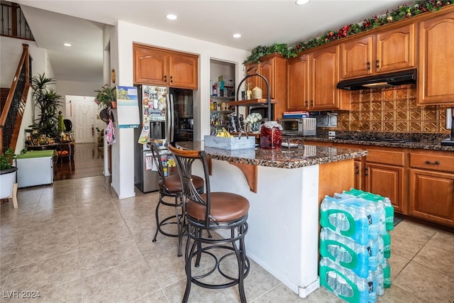 kitchen with stainless steel fridge with ice dispenser, a center island, dark stone countertops, black stovetop, and decorative backsplash