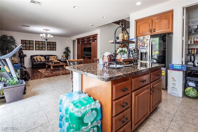 kitchen featuring stainless steel fridge, light tile patterned floors, a kitchen island, dark stone countertops, and a notable chandelier