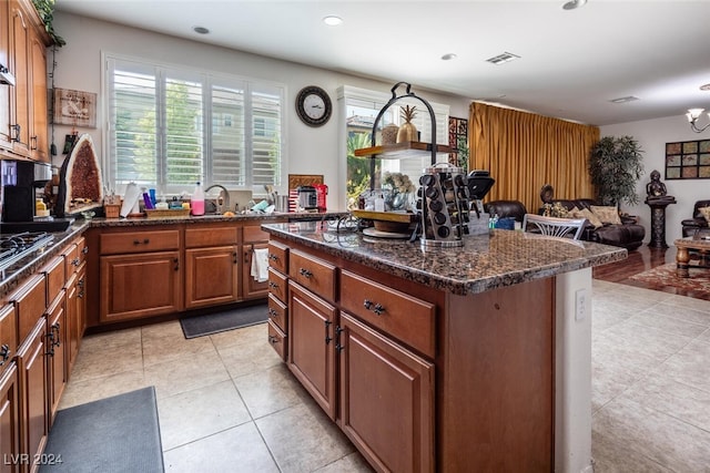 kitchen featuring stainless steel gas stovetop, light tile patterned flooring, dark stone counters, and a kitchen island