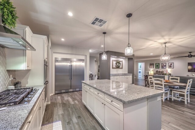 kitchen featuring light wood-type flooring, appliances with stainless steel finishes, backsplash, white cabinets, and wall chimney range hood