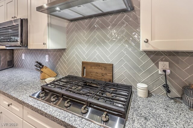 kitchen with stainless steel gas cooktop, backsplash, white cabinets, and custom range hood