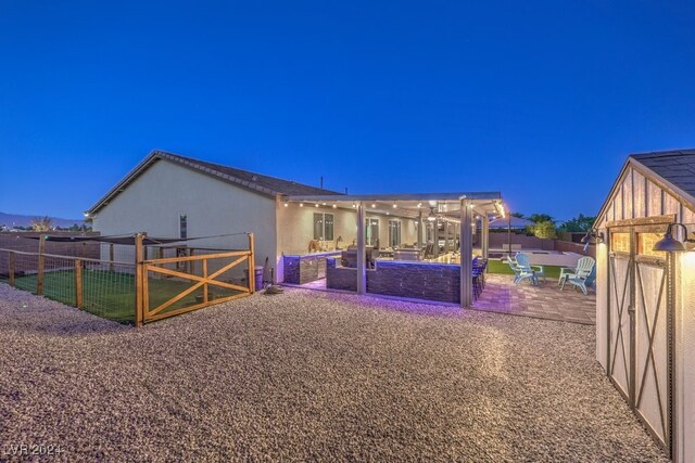 back house at twilight featuring a pergola and a patio