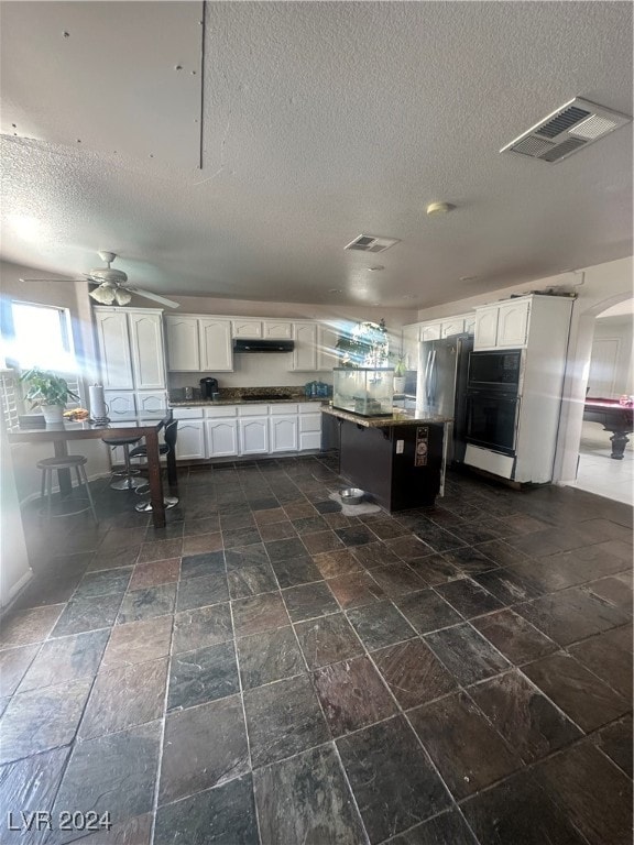 kitchen featuring a textured ceiling, ceiling fan, dark tile patterned floors, white cabinetry, and stainless steel fridge