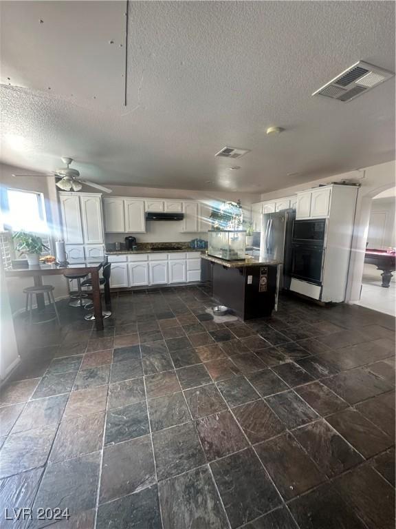 kitchen with white cabinetry, a textured ceiling, stainless steel refrigerator, black oven, and ceiling fan