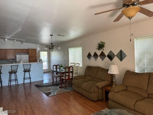 living room featuring rail lighting, dark wood-type flooring, and ceiling fan with notable chandelier