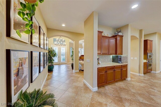 kitchen featuring french doors, an inviting chandelier, light tile patterned flooring, stainless steel double oven, and backsplash