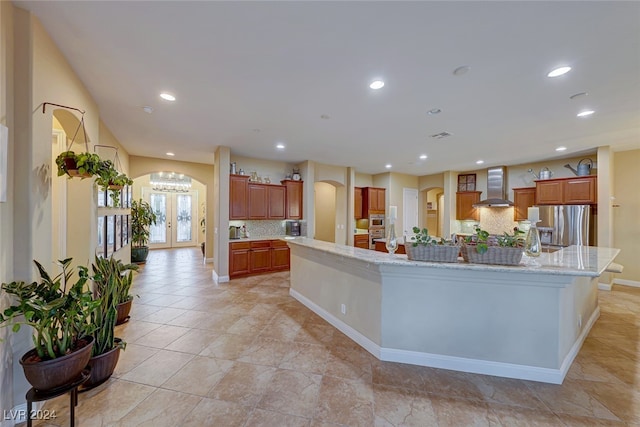 kitchen featuring stainless steel fridge with ice dispenser, tasteful backsplash, a large island, and wall chimney range hood