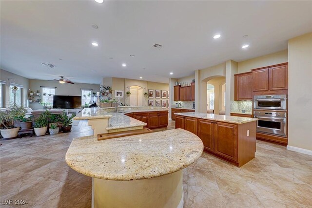 kitchen featuring a spacious island, tasteful backsplash, light stone countertops, and ceiling fan