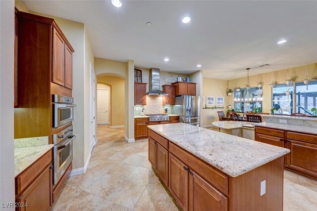 kitchen with appliances with stainless steel finishes, a kitchen island, light tile patterned flooring, light stone counters, and wall chimney range hood