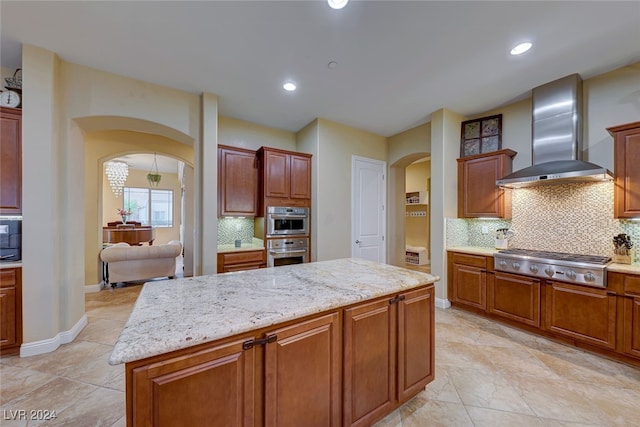 kitchen featuring wall chimney exhaust hood, backsplash, stainless steel appliances, and a kitchen island