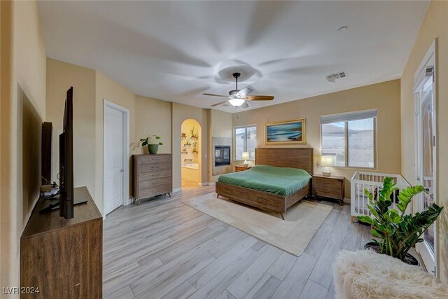 bedroom featuring ceiling fan, light wood-type flooring, ensuite bathroom, and a fireplace