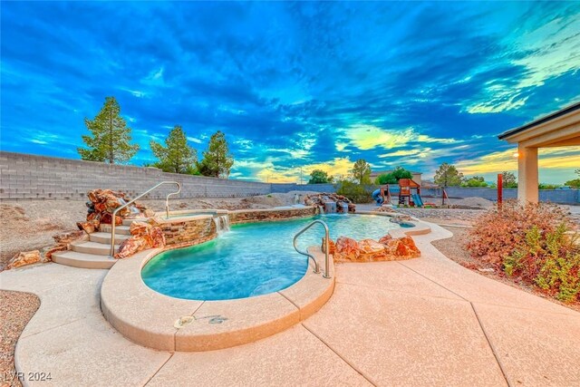 pool at dusk with pool water feature and a patio