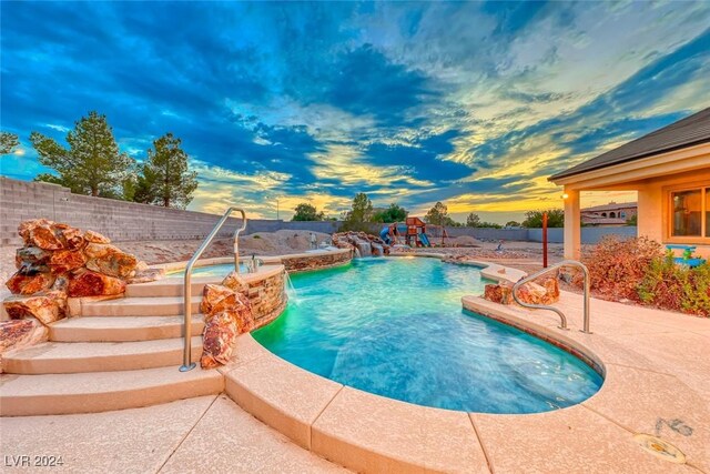 pool at dusk featuring a playground, pool water feature, and a patio area