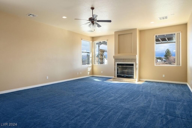 unfurnished living room featuring a tiled fireplace, ceiling fan, and dark colored carpet