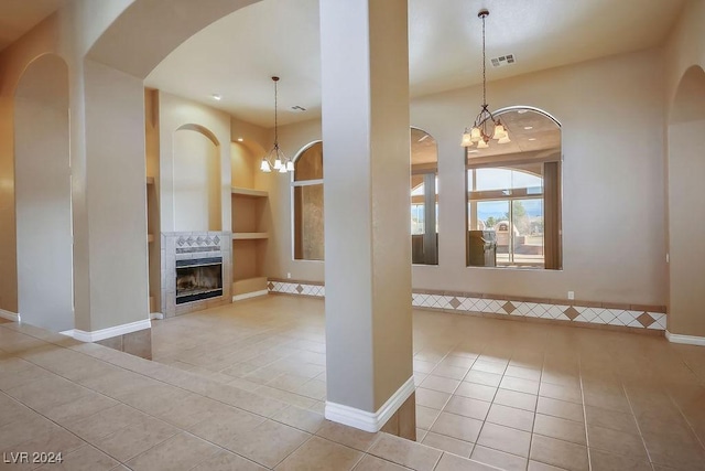 interior space featuring a tile fireplace, light tile patterned floors, built in features, and a notable chandelier