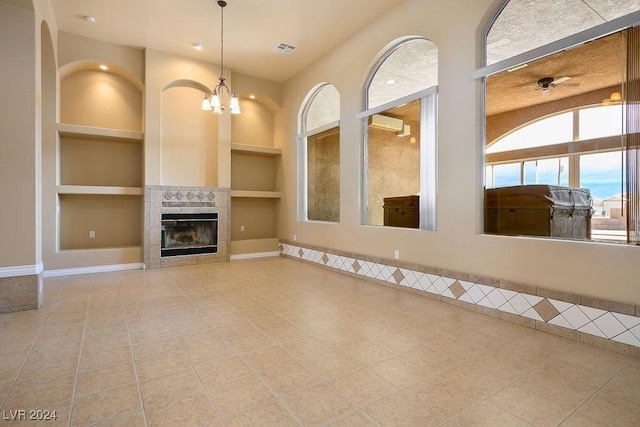 unfurnished living room with a notable chandelier, a tile fireplace, built in features, and tile patterned floors