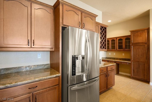 kitchen featuring stone countertops, built in desk, stainless steel fridge with ice dispenser, and light tile patterned floors