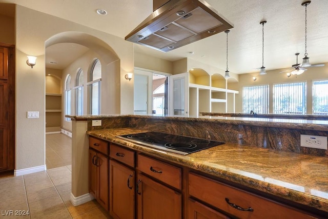 kitchen with light tile patterned floors, hanging light fixtures, range hood, black electric cooktop, and dark stone counters