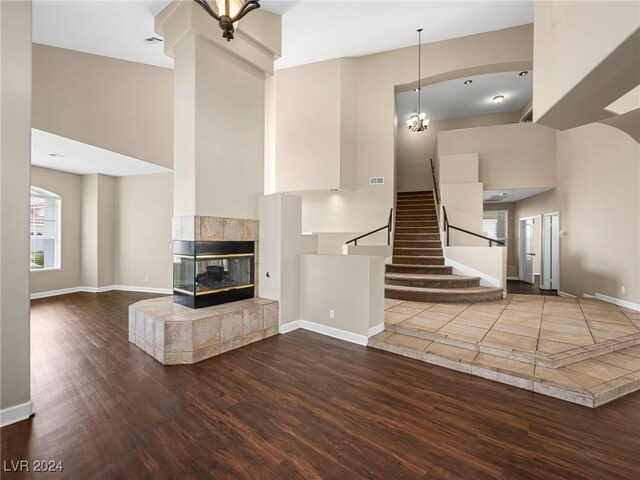 unfurnished living room featuring a tiled fireplace, a towering ceiling, and wood-type flooring