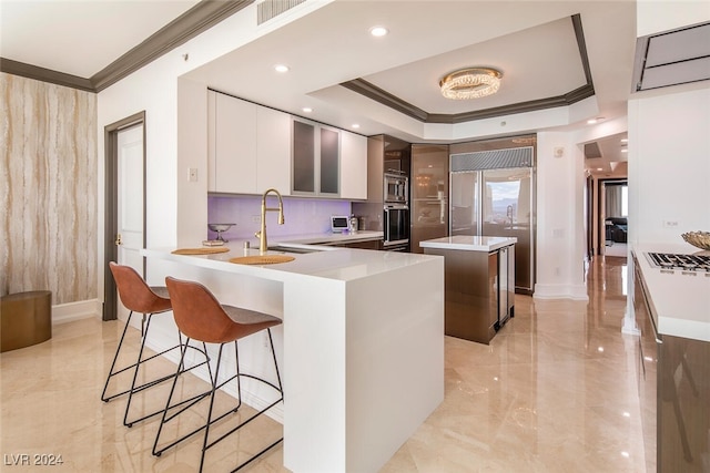 kitchen with a raised ceiling, light tile patterned floors, ornamental molding, a kitchen island, and sink