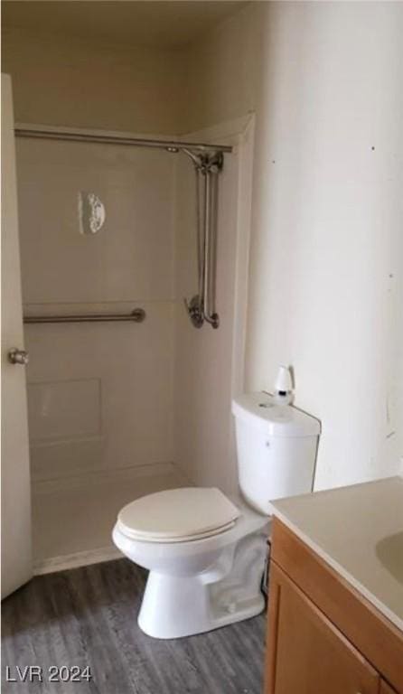 bathroom featuring wood-type flooring, toilet, vanity, and a shower