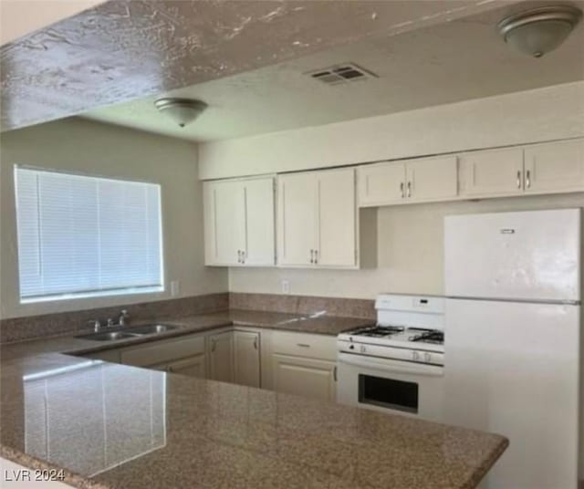 kitchen with sink, white cabinetry, dark stone countertops, kitchen peninsula, and white appliances