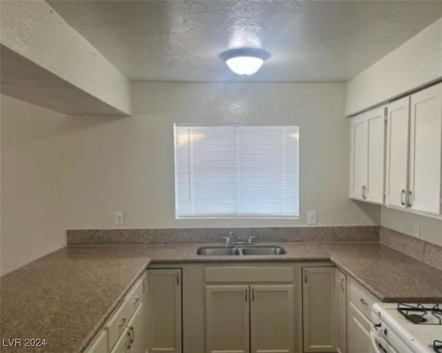 kitchen featuring white range with gas cooktop, sink, and white cabinets