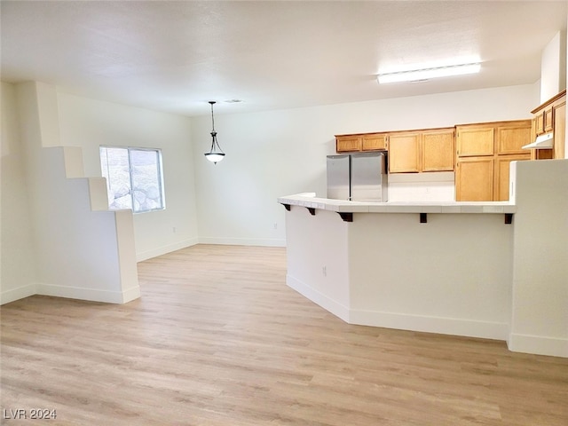 kitchen featuring kitchen peninsula, stainless steel refrigerator, hanging light fixtures, light hardwood / wood-style floors, and tile countertops