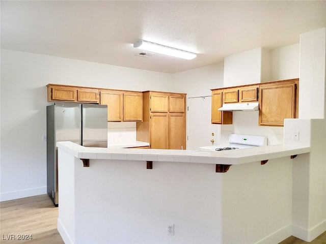 kitchen with tile counters, light hardwood / wood-style flooring, stove, and a breakfast bar