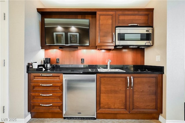 bar featuring refrigerator, a sink, baseboards, stainless steel microwave, and indoor wet bar